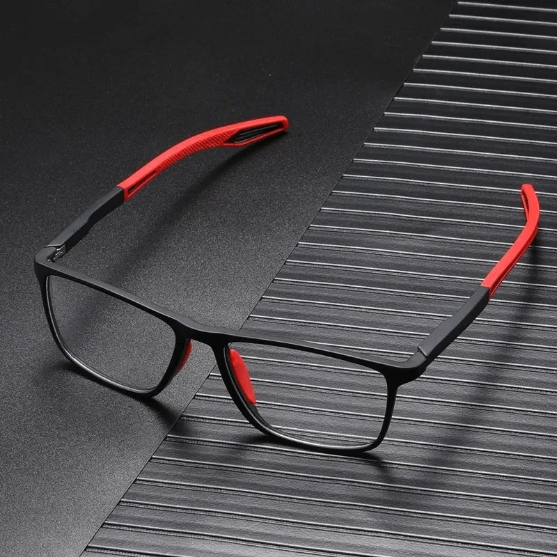 A pair of black reading glasses with red accents resting on a dark, textured surface.