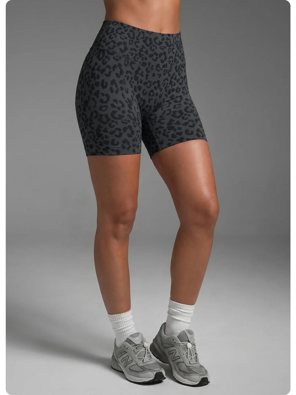 Une femme portant des shorts de yoga à taille haute à imprimé léopard et des baskets grises.