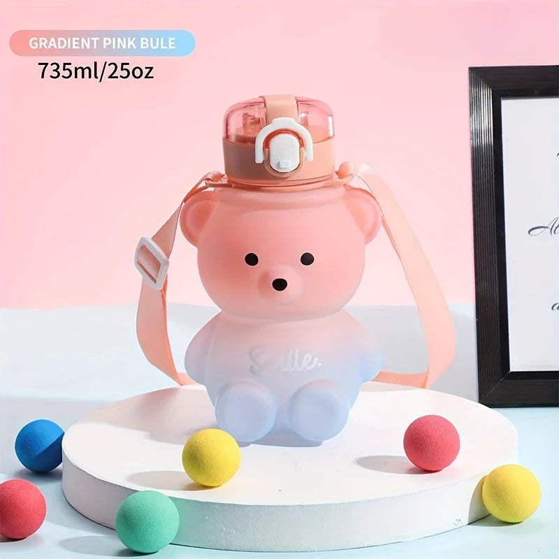 A gradient pink bear-shaped water bottle with a straw and strap sitting on a white stand.
