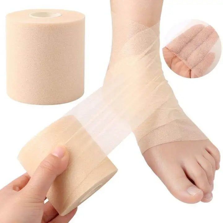 A hand is applying a roll of beige foam athletic tape wrap around a foot and ankle.