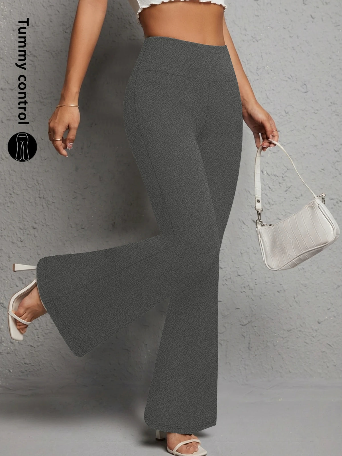 A woman wearing gray flared yoga trousers and a white shoulder bag.