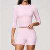 A woman wearing a light pink long-sleeved top and matching high-waisted leggings set for yoga or fitness.