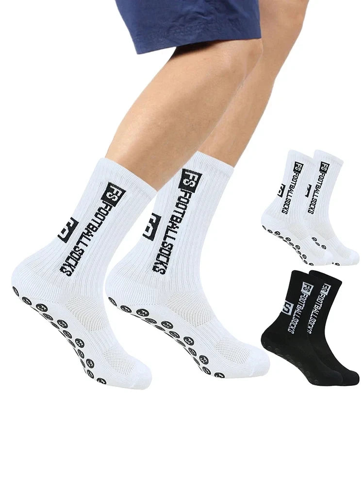 A pair of white men's athletic soccer socks with non-slip grip and black accents are displayed on a person's leg.