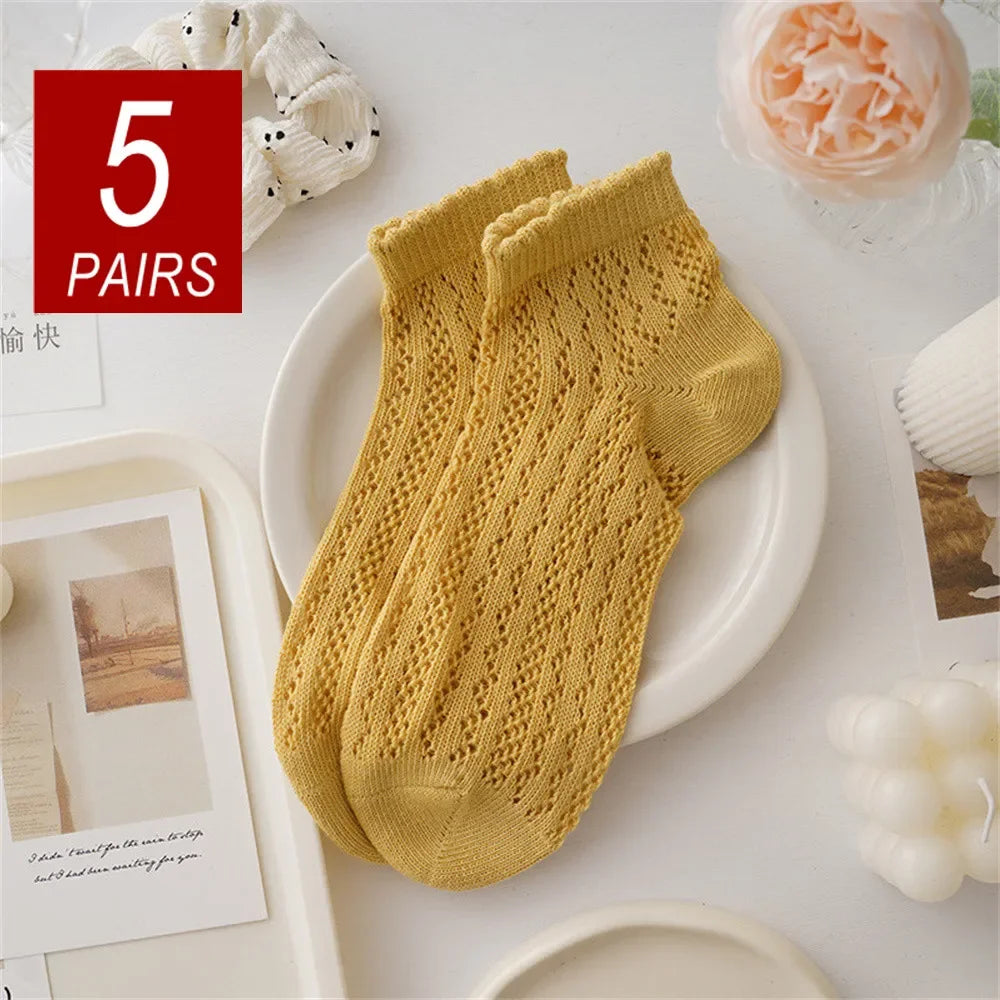 Five pairs of yellow knitted mesh lace tube socks displayed on a white plate.