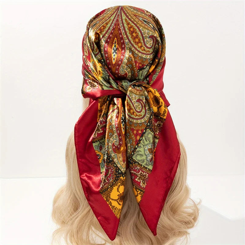 A red satin square scarf with an ornate paisley pattern tied around a blonde wig.