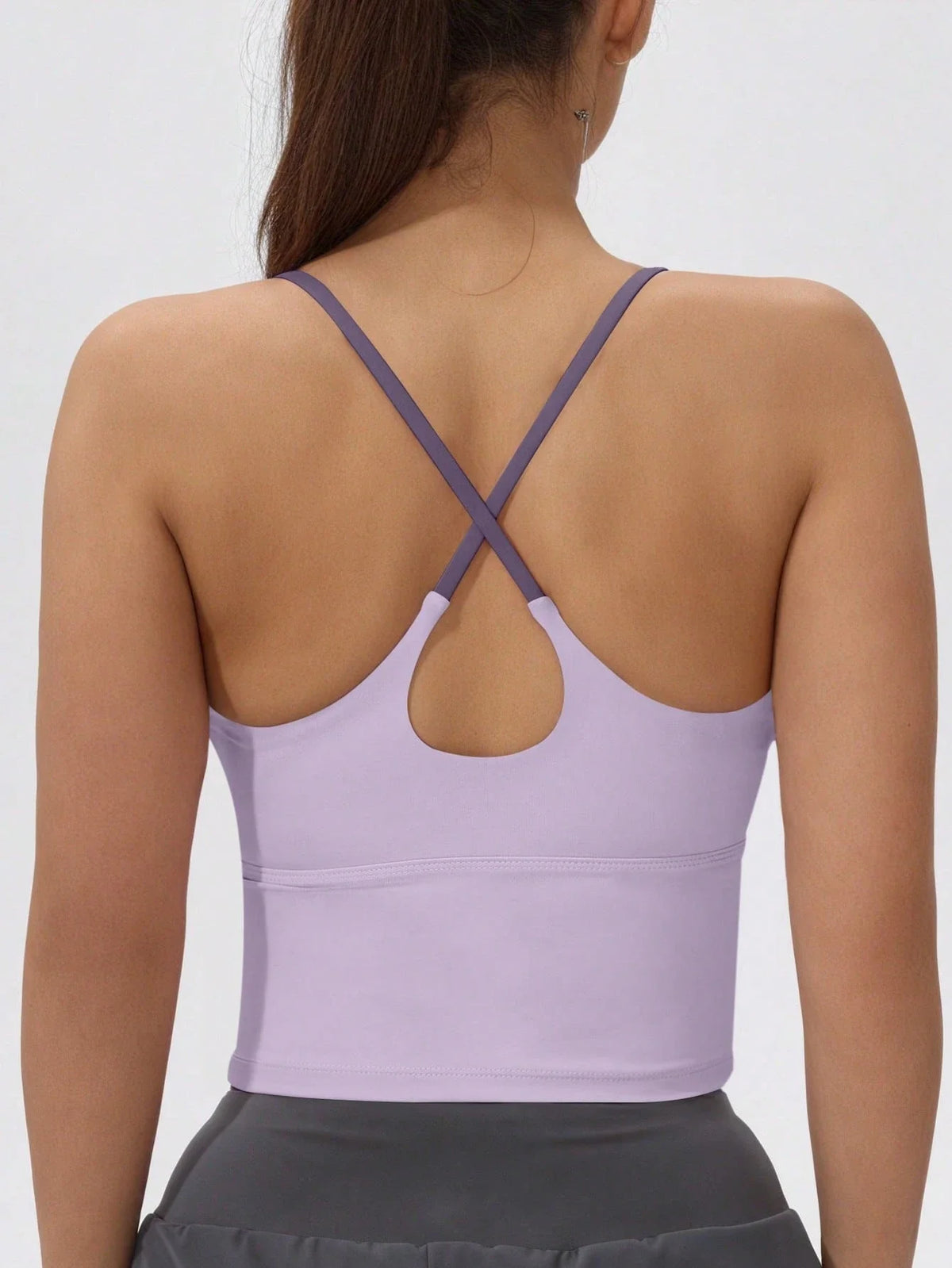 Back view of a purple women's athletic crisscross tank top worn over a gray skirt.