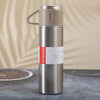 A silver stainless steel vacuum flask with a beige handle and red Hot&Cold markings sits on a dark surface.