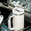 A white silicone butterfly straw cover is placed on a tumbler in a car interior setting.