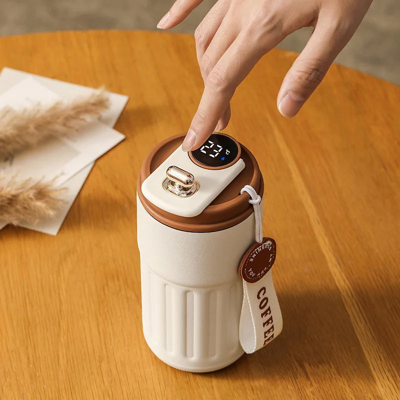 A hand is placing a finger on the display of a white insulated thermos bottle with a digital temperature reading.