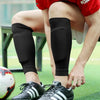 A person wearing black compression socks is kneeling on a green field with a soccer ball nearby.