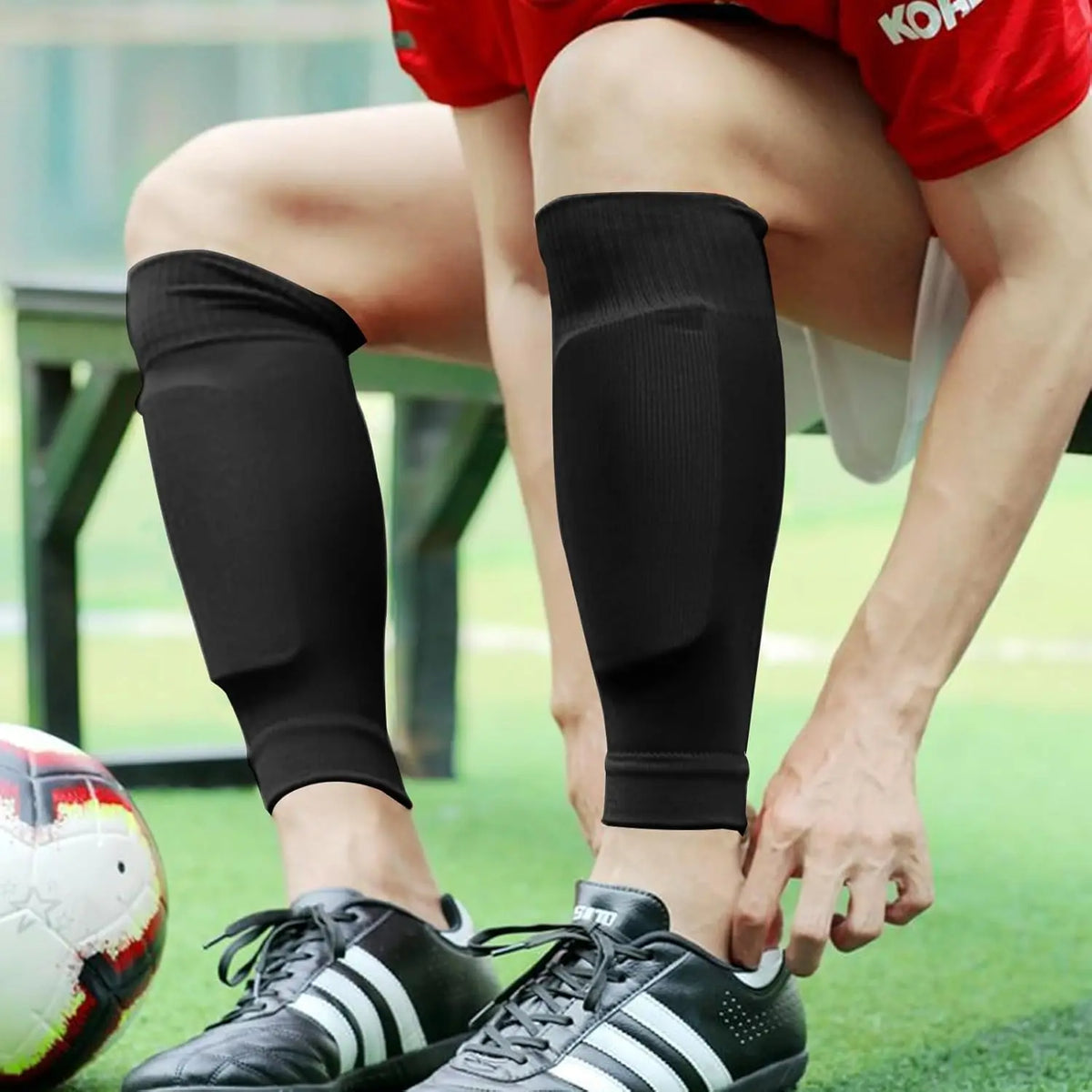 A person wearing black compression socks is kneeling on a green field with a soccer ball nearby.