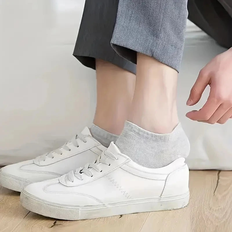 A pair of white canvas sneakers resting on a wooden floor next to a gray ankle sock.
