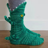 A green knit sock shaped like a crocodile with a yellow eye
