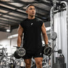 A muscular man wearing a black sleeveless fitness tank and shorts is standing in a gym setting.