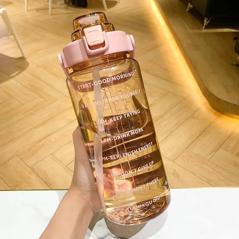 Une main tient une grande bouteille d'eau sportive avec marqueurs de temps, à couvercle rose et liquide ambré.