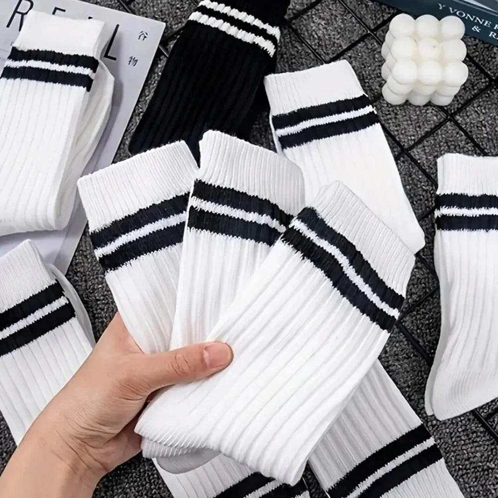 Eine Hand hält einen Stapel aus weiß-schwarz gestreiften, atmungsaktiven Socken auf einer dunklen Oberfläche.