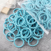 A pile of light blue elastic hair bands, some wrapped in clear plastic, scattered on a gray surface.
