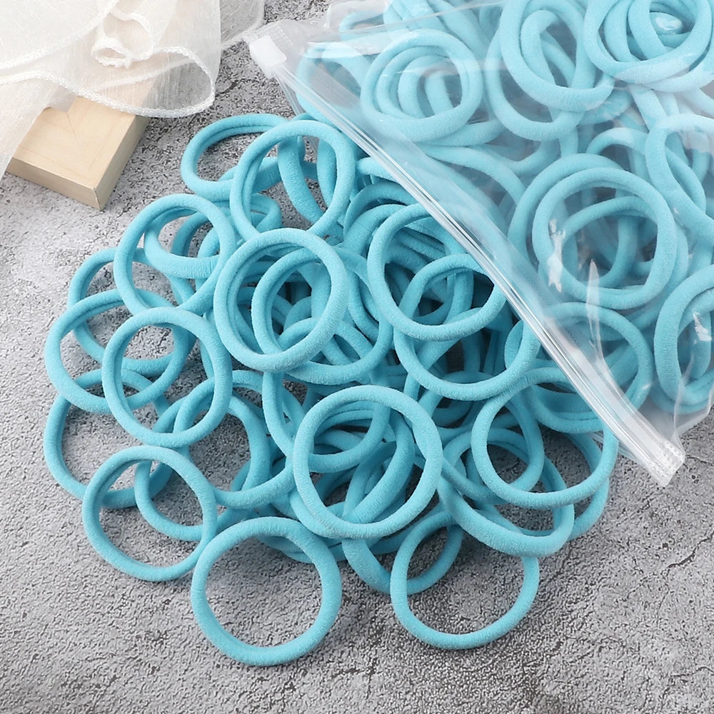 A pile of light blue elastic hair bands, some wrapped in clear plastic, scattered on a gray surface.