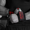 Gros plan d'une main agrippant des bandelettes de poignet de musculation noires avec des accents rouges.