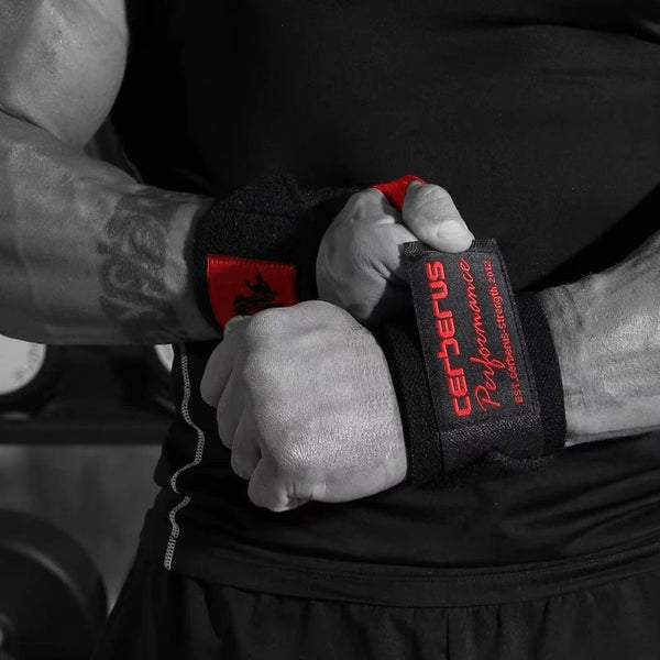 A close-up shot of a person's hand gripping black weightlifting wrist wraps with red accents.