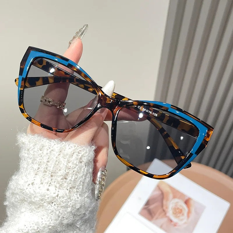 A hand holds a pair of vintage square cat eye sunglasses with brown and black leopard print frames.