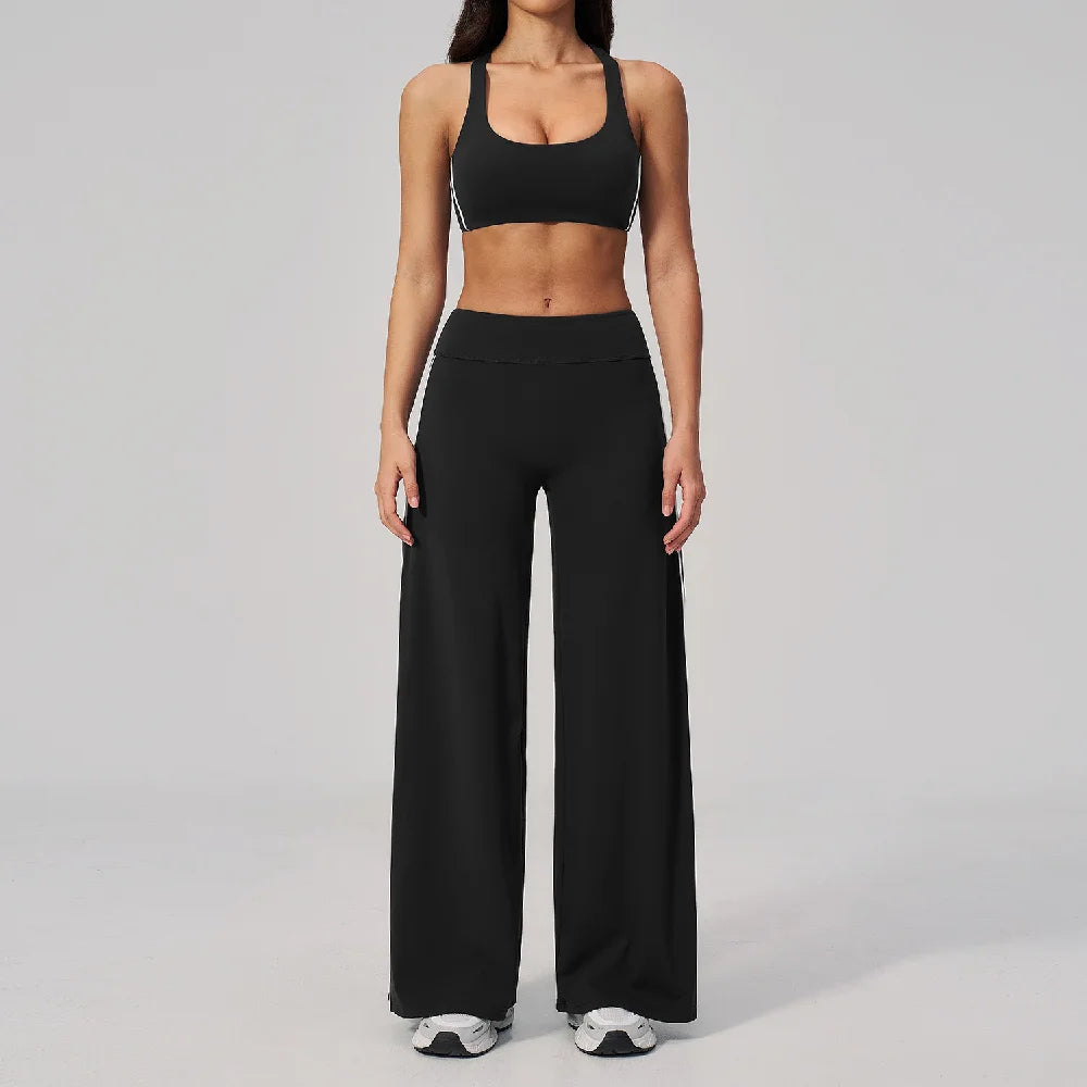 A woman wearing a black two-piece yoga and sports tracksuit set consisting of a cropped top and loose pants.