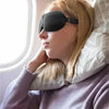 A woman wearing a black light blocking sleep mask is resting near a window.