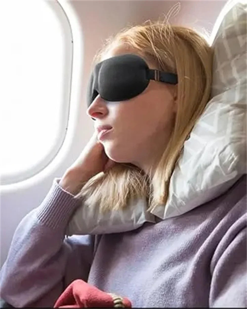 A woman wearing a black light blocking sleep mask is resting near a window.