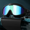 A pair of black swimming goggles with blue-tinted lenses resting on a teal fabric.