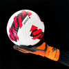 A close-up of a white soccer ball with red and black graphics, held by an orange goalkeeper glove.