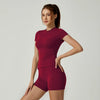 Una mujer modela un conjunto de yoga color granate de talle alto, con una blusa de manga corta y shorts a juego.