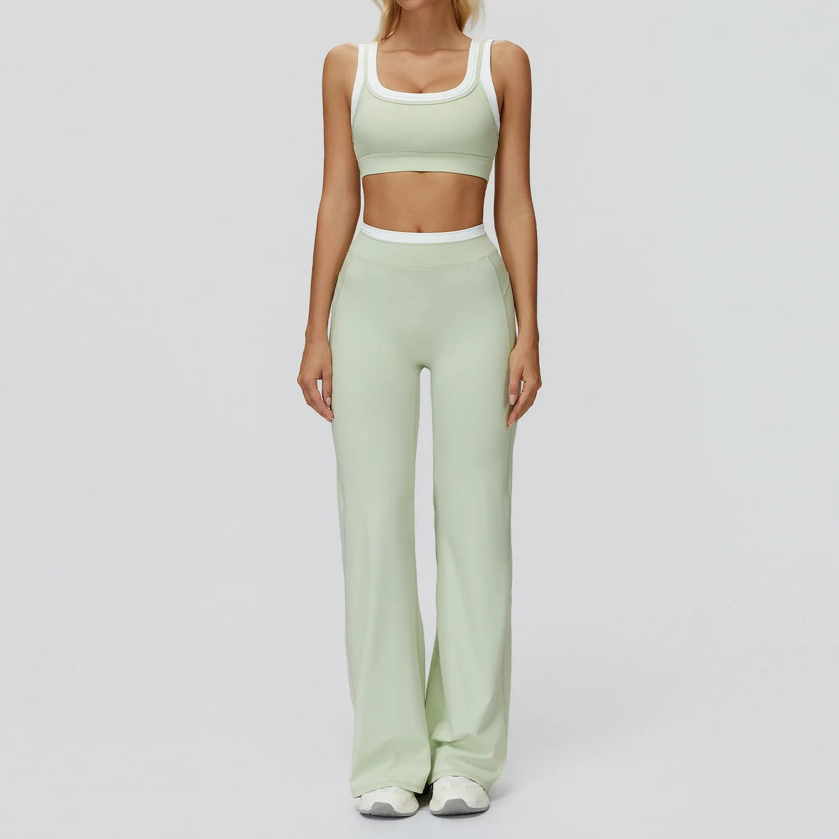 Eine Frau trägt ein hellsalbegrünes zwei-teiliges Yoga- und Gym-Trainingsanzug mit cropped Top und passenden langen Hosen.