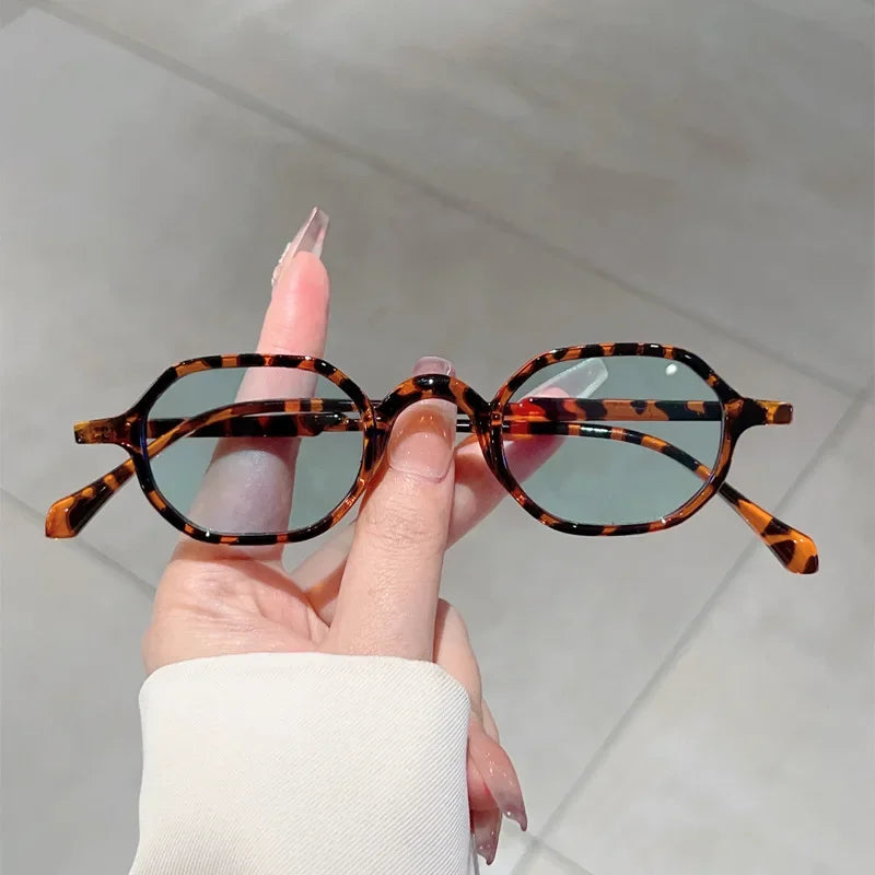 A hand holds a pair of vintage oval sunglasses with an orange and black leopard print pattern.