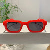 A pair of bright red, square-shaped sunglasses resting on a white surface.