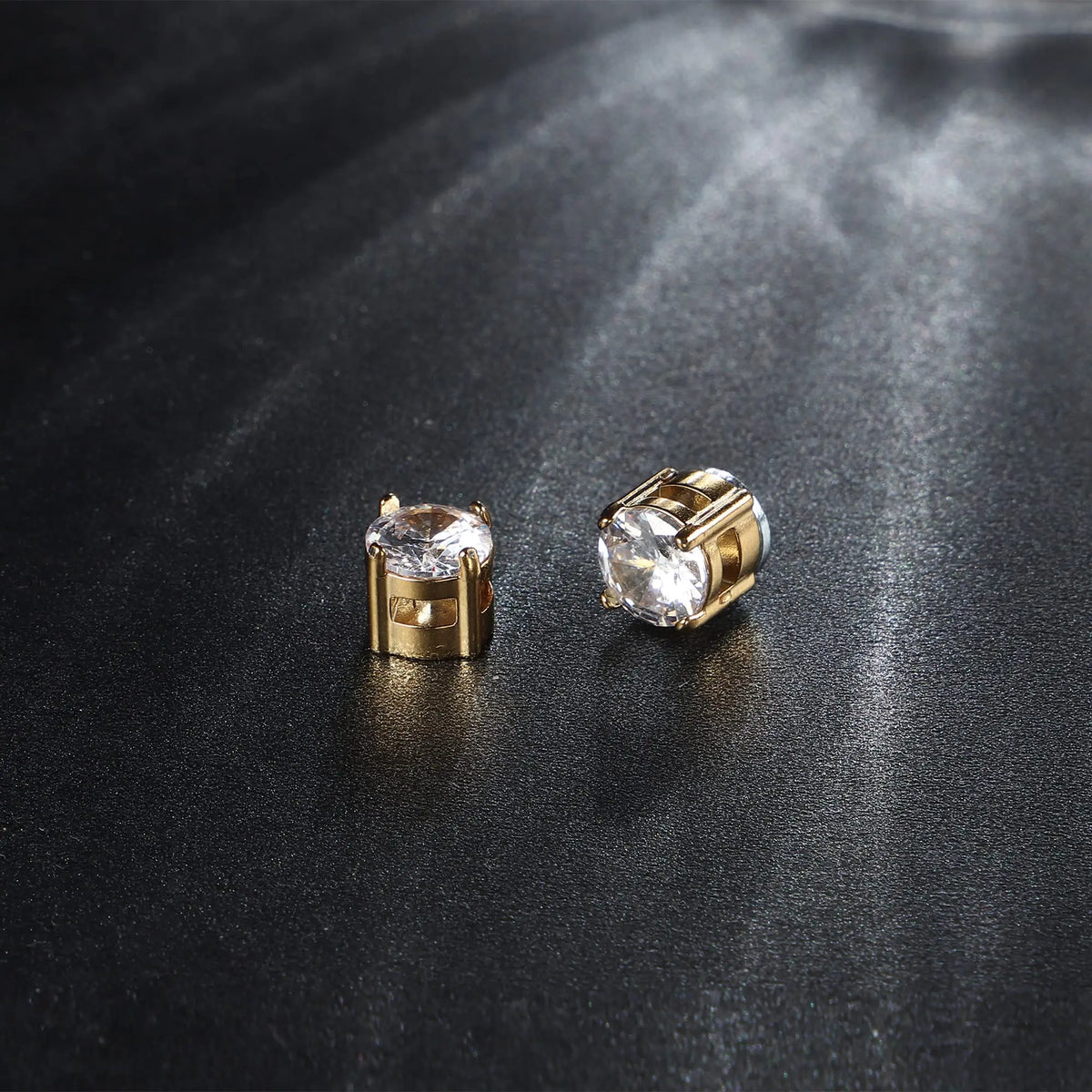 A pair of gold-toned magnetic cubic zirconia stud earrings resting on a dark surface.