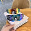 A pair of mirrored cycling sunglasses resting on a white book on a wooden table.