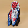 A vibrant red and blue floral satin square scarf tied around a person's hair.