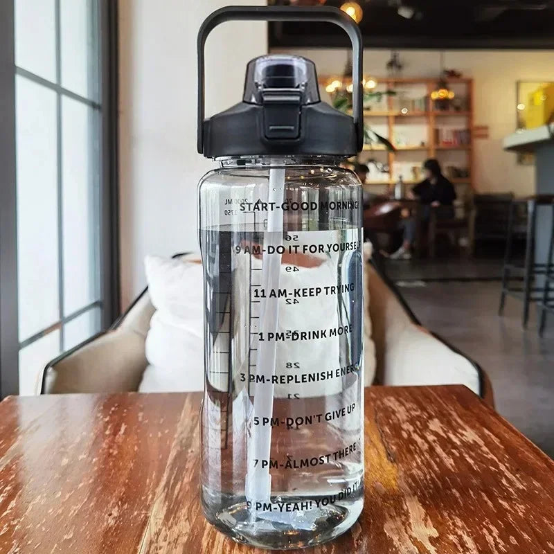 A clear insulated water bottle with a black lid and straw is placed on a wooden table.