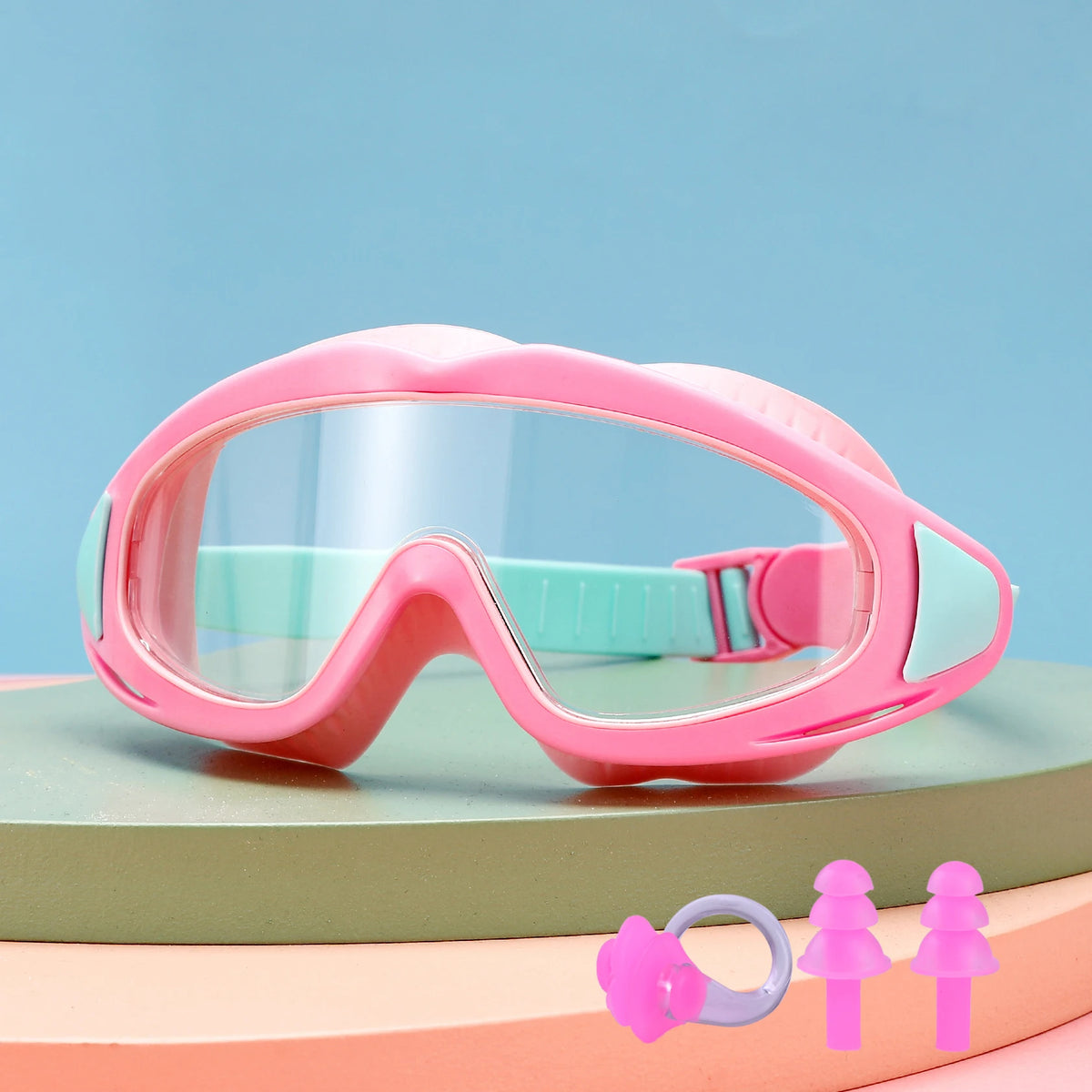 Pink swimming goggles for children resting on a green surface with small pink toys.