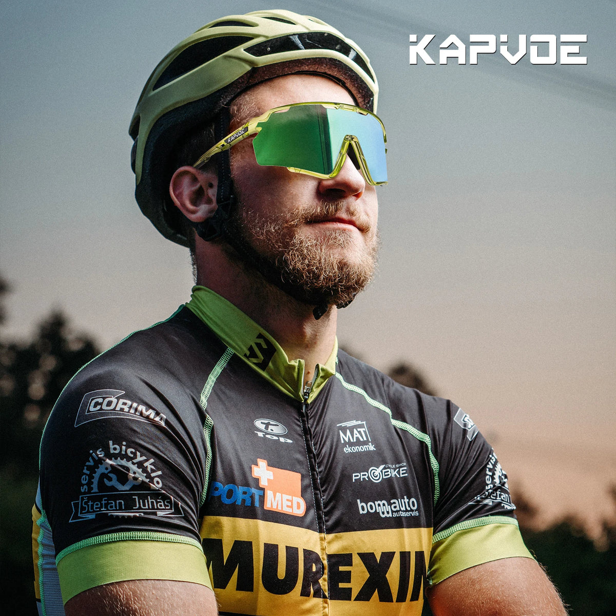 A bearded man wearing yellow photochromic cycling sunglasses and a green helmet, looking to the side.