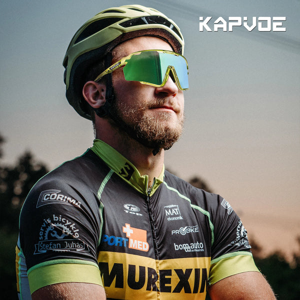 A bearded man wearing yellow photochromic cycling sunglasses and a green helmet, looking to the side.