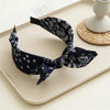 Navy paisley bandana headband folded and displayed on a light tray next to a woven object.