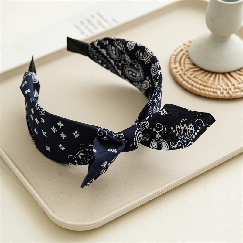 Navy paisley bandana headband folded and displayed on a light tray next to a woven object.
