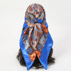 An elegant blue satin square scarf featuring an orange and blue paisley pattern tied around dark hair.