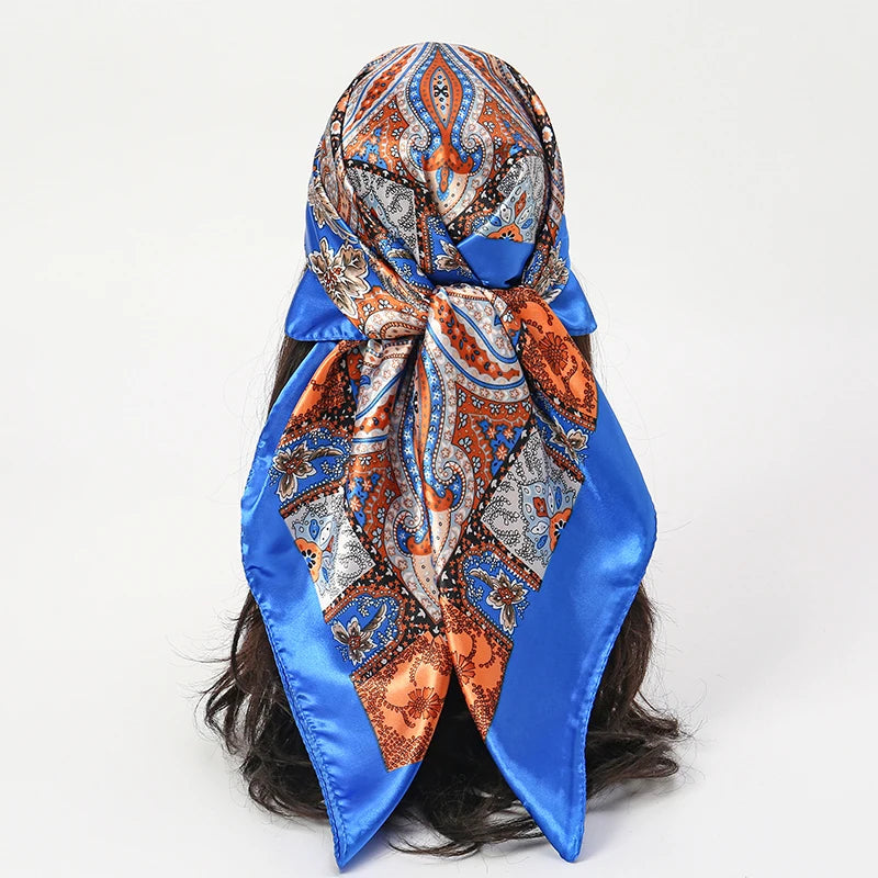 An elegant blue satin square scarf featuring an orange and blue paisley pattern tied around dark hair.