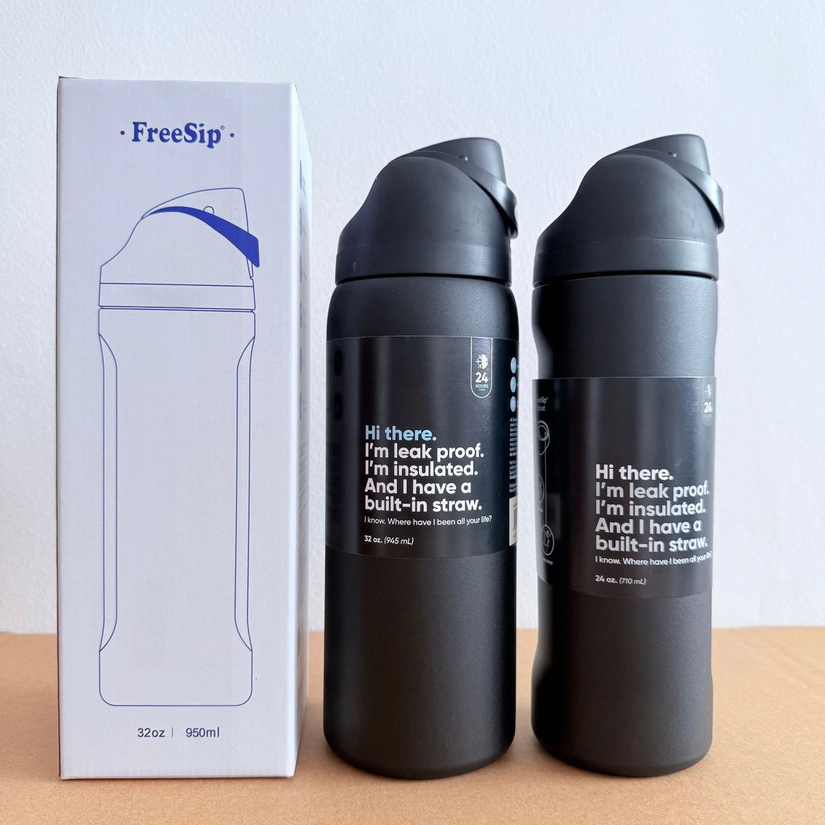 A black stainless steel vacuum insulated water bottle with a straw is shown next to its packaging.