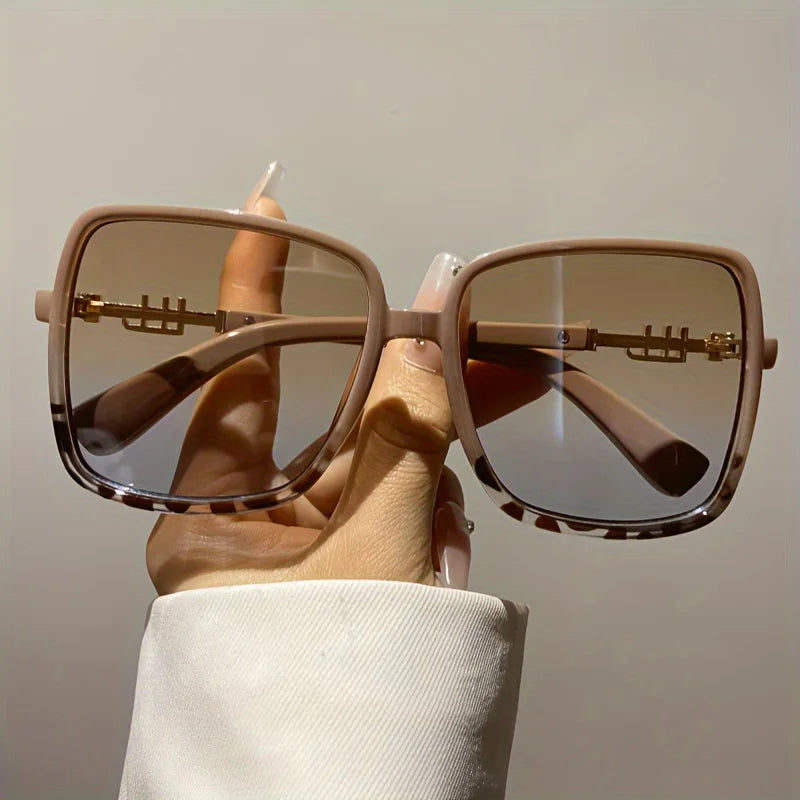A hand holds a pair of retro two-tone gradient sunglasses with light brown frames and tinted lenses.