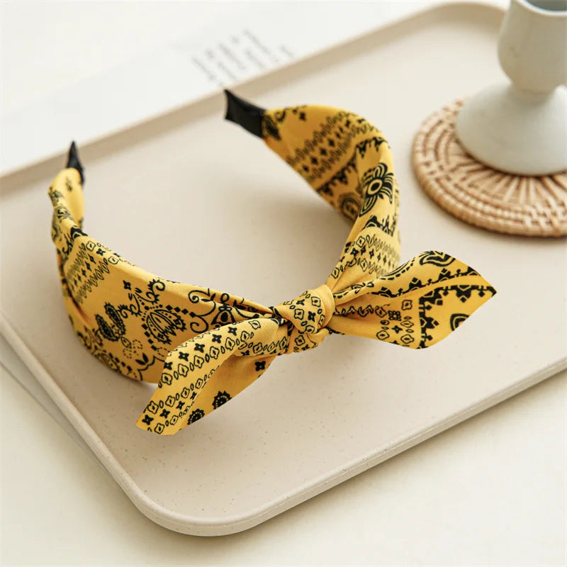 Yellow paisley bandana headband tied in a bow displayed on a light tray.