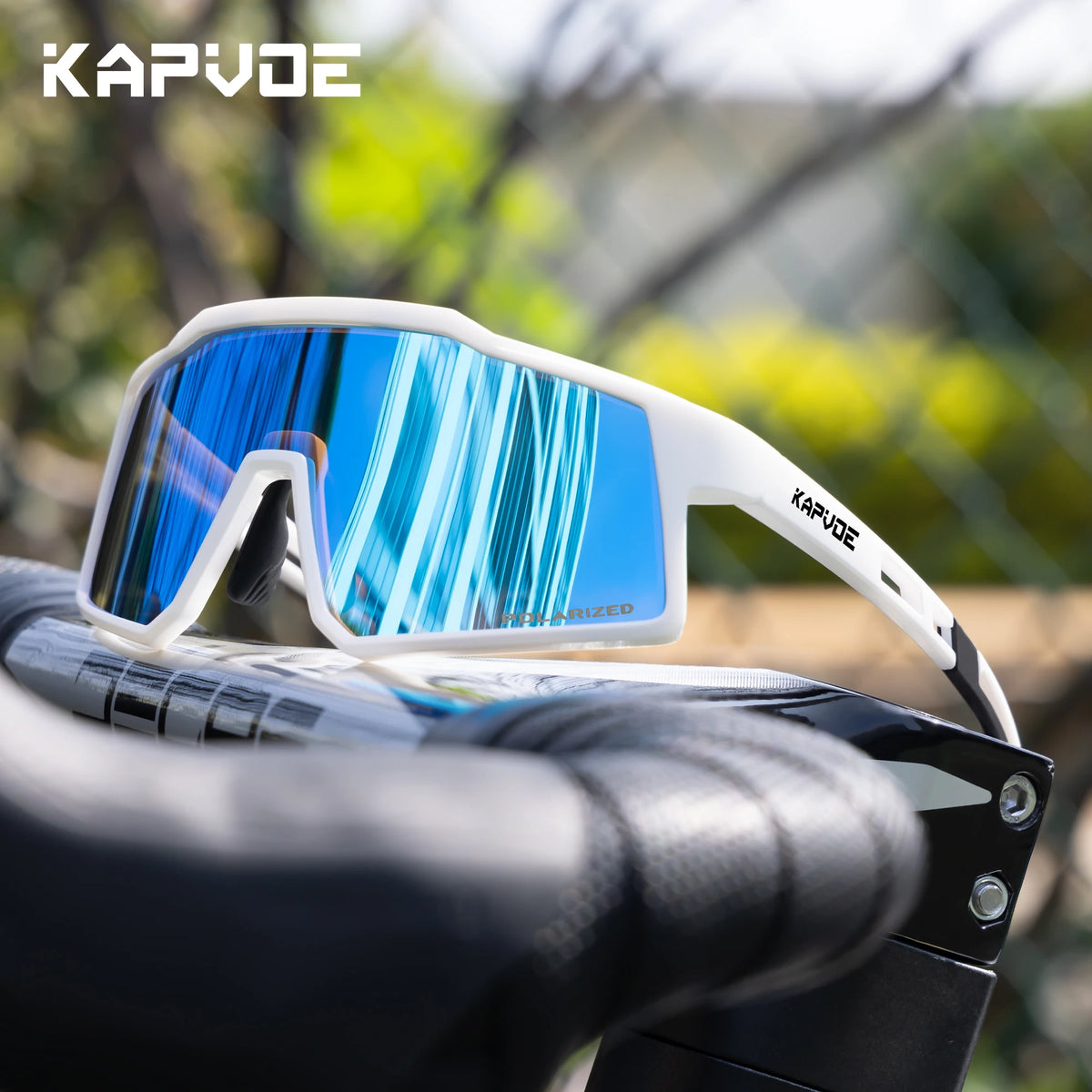 A pair of white Kapvode polarized sports sunglasses with blue mirrored lenses resting on a black sports grip.
