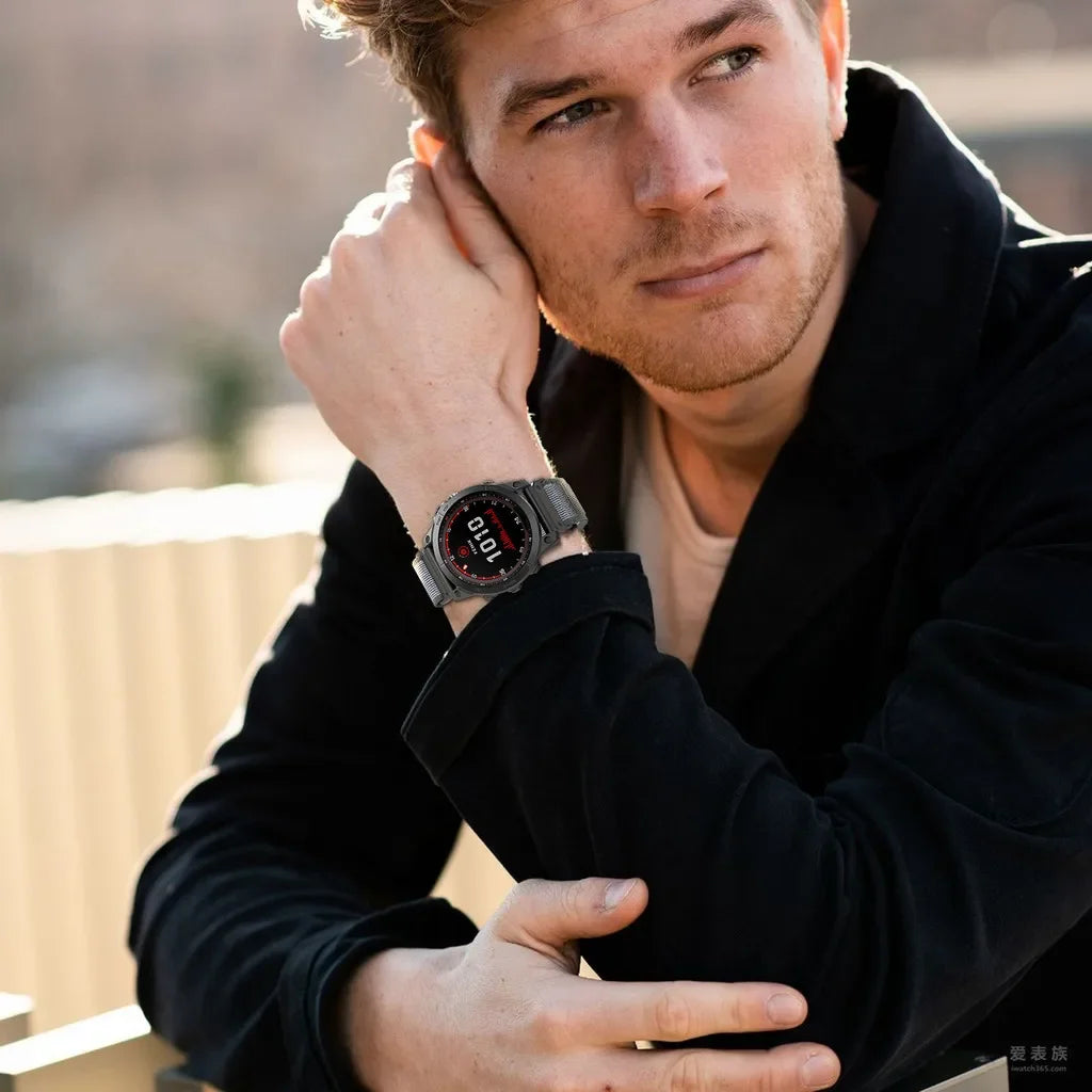 A man wearing a black jacket is looking off-camera while touching his wrist, showing an adjustable nylon strap for a Garmin s
